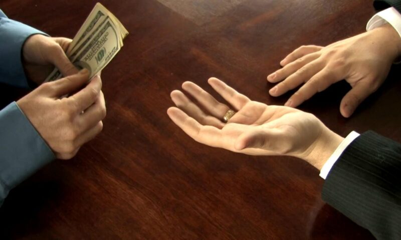 dve osobe na slici, prikaz njihovih ruku, jedna osoba predaje drugoj novac