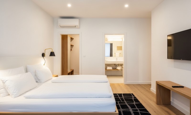 Moderna hotelska soba sa bračnim krevetom, belom posteljinom, zidnim televizorom i drvenim stolom