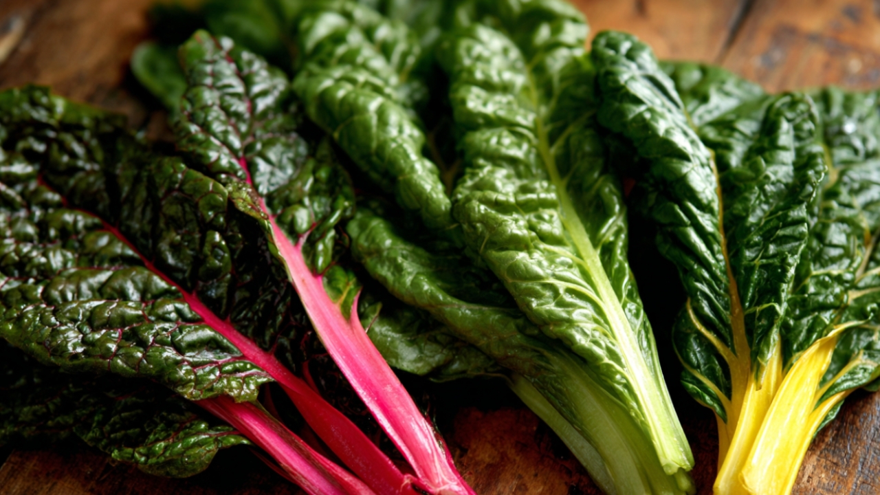 Sveže tamnozeleno povrće poput blitve i lisnatih salata na drvenoj podlozi