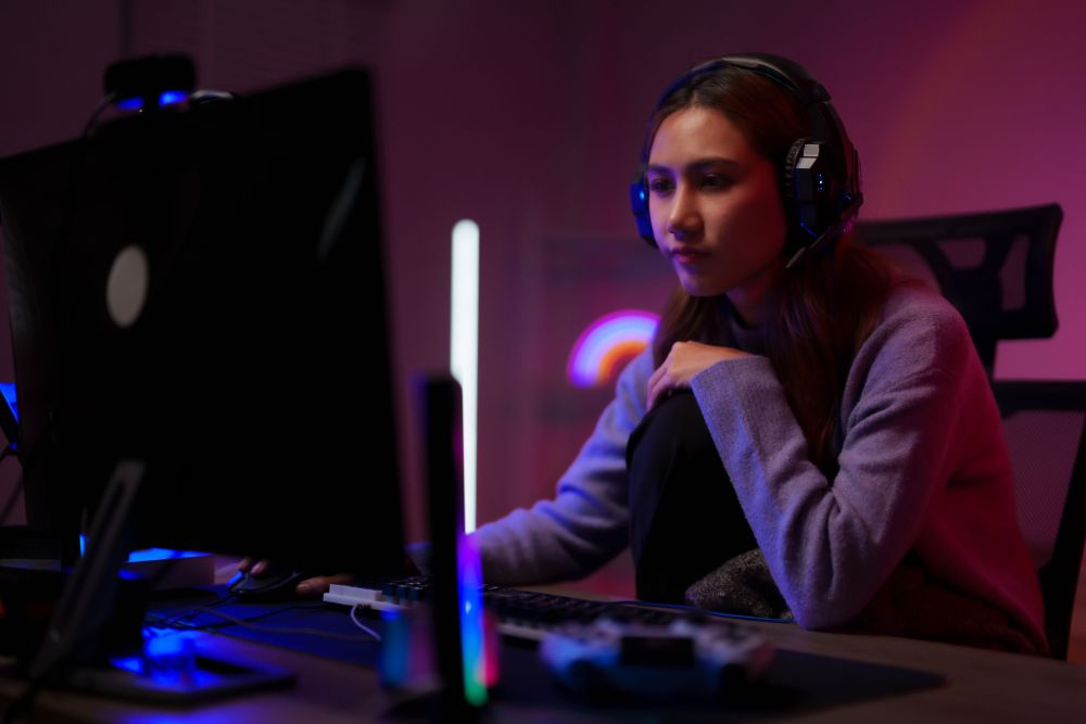 Gejmerka sa slušalicama zamišljeno posmatra monitor u prostoru osvetljenom RGB rasvetom.